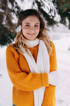 Teen blonde in a yellow sweater outside in winter. A teenage girl on a walk in winter clothes in a snowy forest.