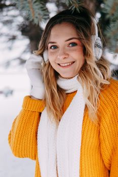 Teen blonde in a yellow sweater outside in winter. A teenage girl on a walk in winter clothes in a snowy forest.