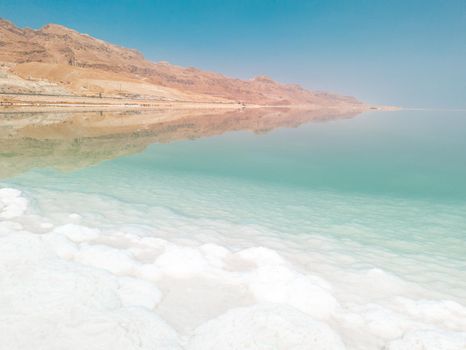 Landscape view on Dead Sea salt crystals formations, clear cyan green calm water and mountains at Ein Bokek beach, Israel