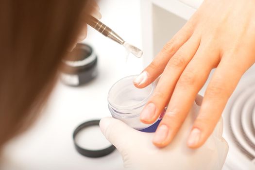 Manicure master applying acrylic powder on the female nails in a beauty salon. Strengthening of nails acrylic powder