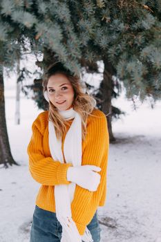 Teen blonde in a yellow sweater outside in winter. A teenage girl on a walk in winter clothes in a snowy forest.