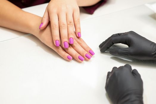 Beautiful fingers with purple nails after nail polish procedure in manicure salon