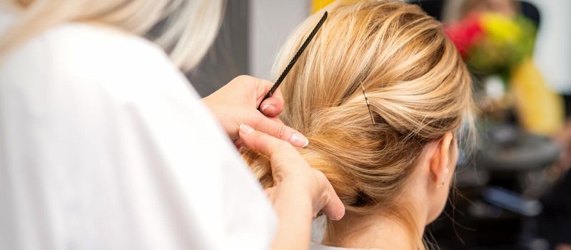 Close-up hairdresser styling blonde hair on the back of the head in a beauty salon