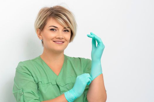 Doctor beautician puts on sterile blue gloves smiling prepares to receive clients on white