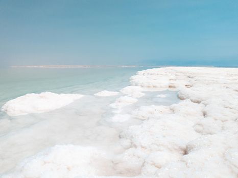 Landscape view on Dead Sea salt crystals formations, clear cyan green calm water at Ein Bokek beach, Israel