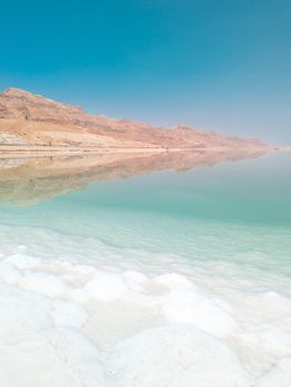 Landscape view on Dead Sea salt crystals formations, clear cyan green calm water and mountains at Ein Bokek beach, Israel