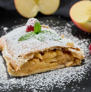 Baked strudel with apples sprinkled with powdered sugar on a black board, delicious dessert