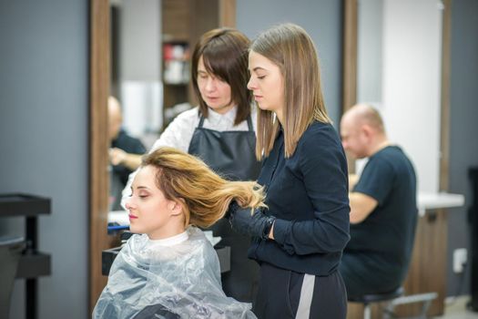 Two female hairstylists prepare long hair of a young woman making curls hairstyle in a beauty salon