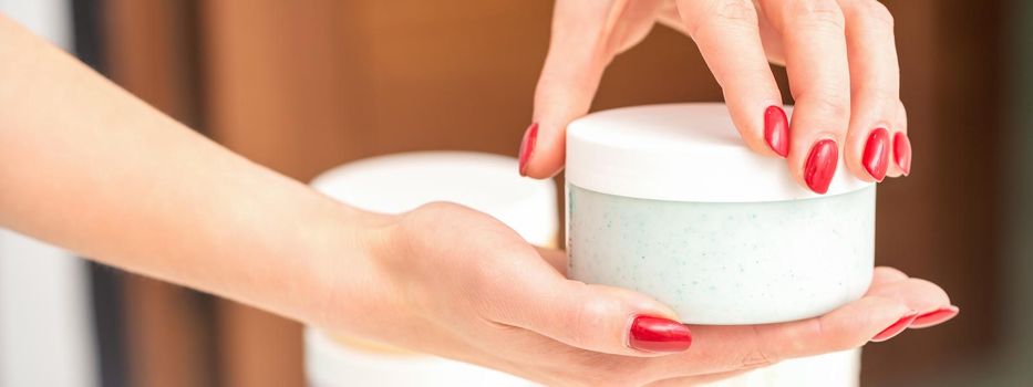 The woman opens the lid holding a jar of moisturizing cream, mockup, copy space, closeup