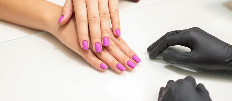 Beautiful fingers with purple nails after nail polish procedure in manicure salon