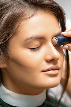 Make up artist contouring the face of a young woman with cream blush close up