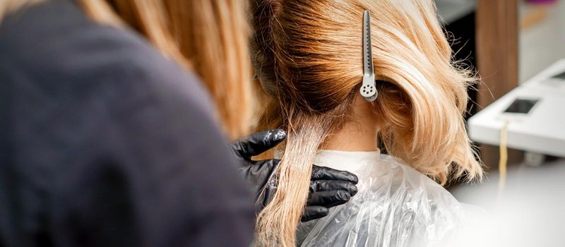 A hairdresser is applying color to the hair of a customer. Hair coloring in a beauty salon. Beauty and people concept. Close-up back view