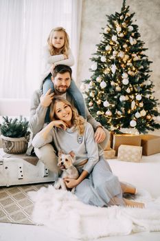 Happy family: mom, dad and pet. Family in a bright New Year's interior with a Christmas tree.