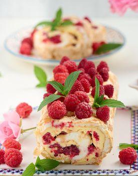 Baked meringue roll with cream and fresh red raspberry on a black wooden board, delicious dessert