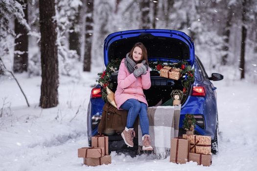 A woman in winter clothes drinks a hot drink sitting in a car decorated in a New Year's way. Traveling by car through the forest. A trip before Christmas.