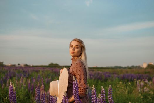 A beautiful woman in a straw hat walks in a field with purple flowers. A walk in nature in the lupin field.