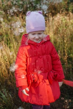 A little girl in a red coat walks in nature in an autumn grove. The season is autumn.