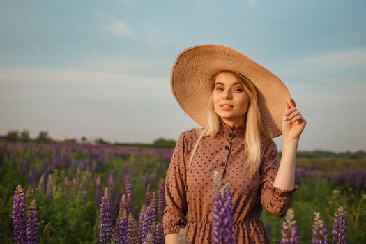 A beautiful woman in a straw hat walks in a field with purple flowers. A walk in nature in the lupin field.