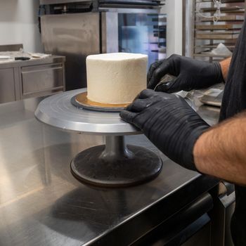 Decorator using spatula and scraper to smooth buttercream on a frosted cake