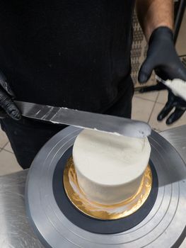 Decorator using spatula and scraper to smooth buttercream on a frosted cake
