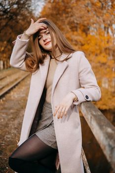 A beautiful long-haired woman walks through the autumn streets. Railway, autumn leaves, a woman in a light coat.