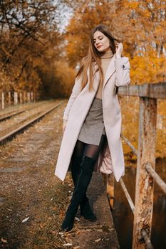 A beautiful long-haired woman walks through the autumn streets. Railway, autumn leaves, a woman in a light coat.