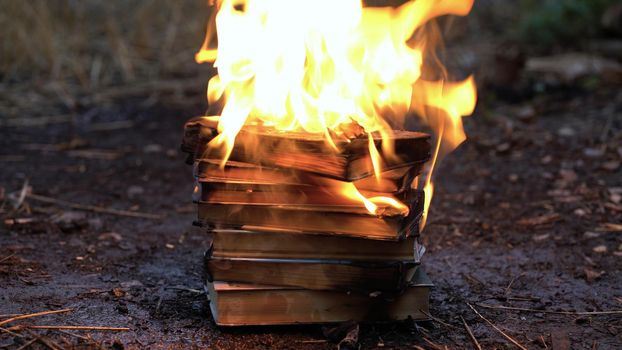 A stack of old books on fire burns on the ground.