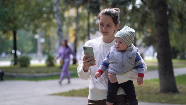 A mother with a child in her arms walking along the path is typing a message on the phone or browsing the news feed.