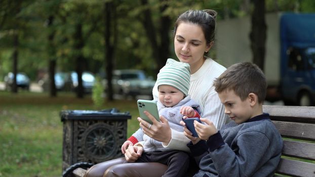 The nanny babysits the children while walking outdoors and playing on the phone.