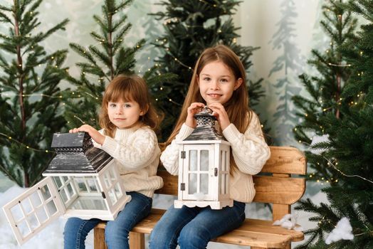 Two cute sisters are sitting in a Christmas interior and holding lanterns