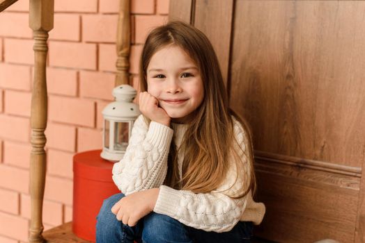 A cute little girl is sitting on the porch of the Christmas door