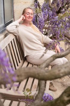 a beautiful middle-aged woman sits on a bench in the thickets of blooming wisteria and meditates happy. High quality photo