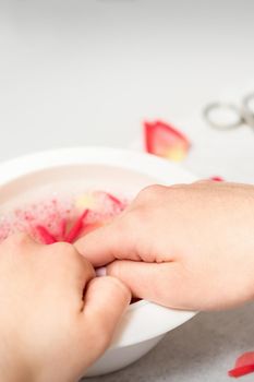 Hands in white bowl bathe nails with water and rose petals to soften the cuticle and dry skin