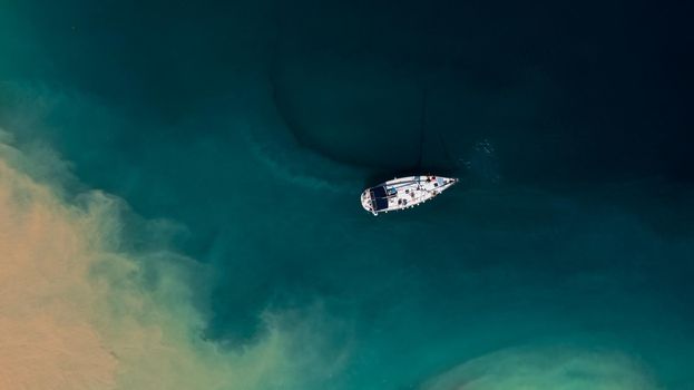 Small white yacht with unrecognizable people in the turquoise sea water, aerial top view