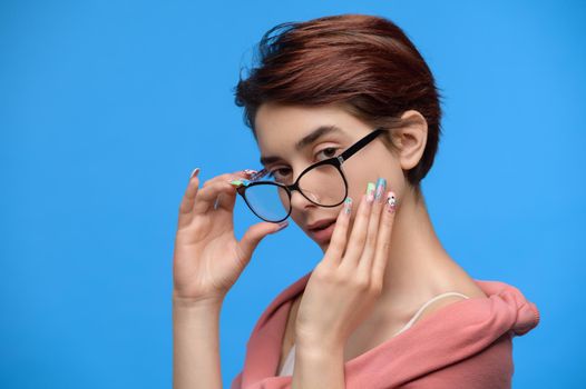 Portrait of young brunette girl with short haircut and extravagant nail art looks over the glasses