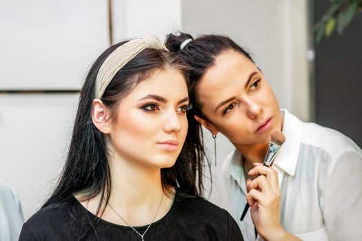 Make-up artist doing makeup for young beautiful bride applying wedding makeup in a beauty salon