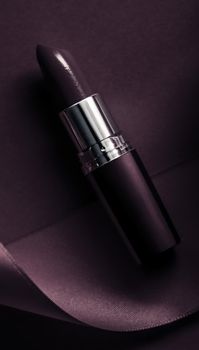 Cosmetic branding, glamour lip gloss and shopping sale concept - Luxury lipstick and silk ribbon on dark purple holiday background, make-up and cosmetics flatlay for beauty brand product design