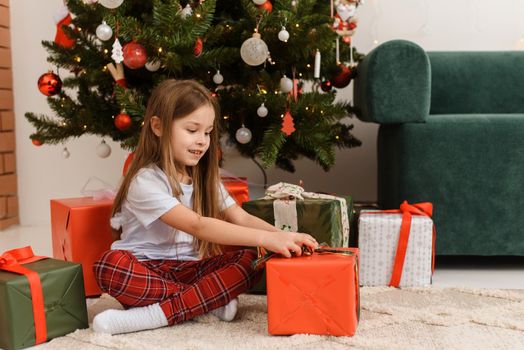 Child girl in pajamas opens a gift on Christmas morning. Happy New Year