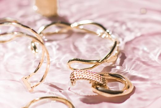 Jewellery branding, fashion gift and luxe shopping concept - Golden bracelets, earrings, rings, jewelery on pink water background, luxury glamour and holiday beauty design for jewelry brand ads