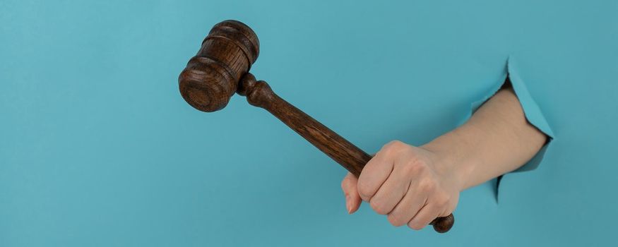 A woman's hand with a wooden judge's gavel sticks out of a hole in a blue background
