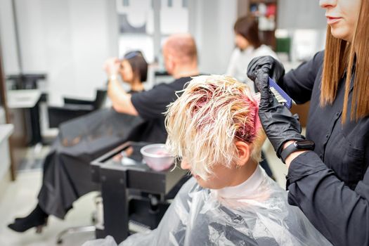 The professional hairdresser uses a brush to apply the pink dye to the hair. Hair coloring concept