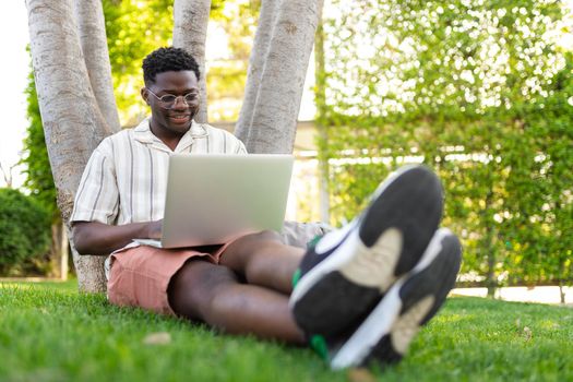 Young black man using laptop in public park. African american male college student doing homework on campus. Copy space. Education and technology concepts.