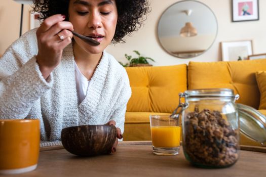 African American woman eating granola for breakfast at home living room. Coffee and orange juice, Copy space. Healthy lifestyle.