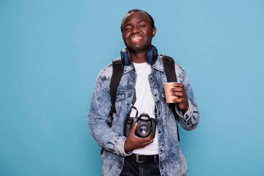 Photography enthusiast with DSLR device and journey rucksack getting ready for vacation journey. Smiling heartily young man having trip backpack and professional camera going on weekend holiday.