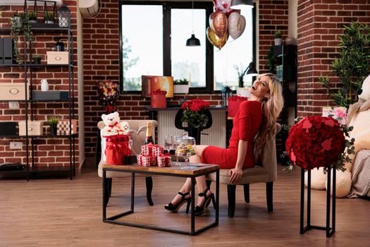 Laughing happy woman sitting in living room with valentines day gifts from boyfriend, girlfriend with luxury presents, bear soft toy, red roses, balloons. February 14 romantic surprises