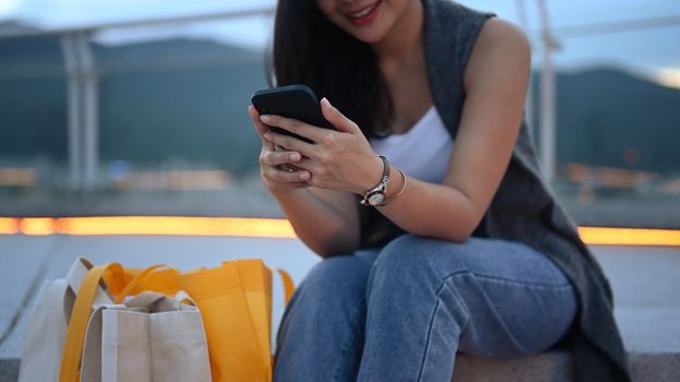 Cropped shot of smiling woman using mobile phone while on stairs at roof terrace outdoors.