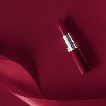 Cosmetic branding, glamour lip gloss and shopping sale concept - Luxury lipstick and silk ribbon on maroon holiday background, make-up and cosmetics flatlay for beauty brand product design