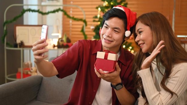 Loving young couple having video call on smart phone, sitting in room decorated for celebrating New year and Christmas festive.