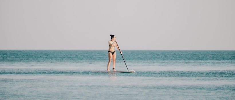 Silhouette of woman standing, surfing on SUP board, confident paddling through water surface. Idyllic sunset or sunrise. Sports active lifestyle at sea or river.
