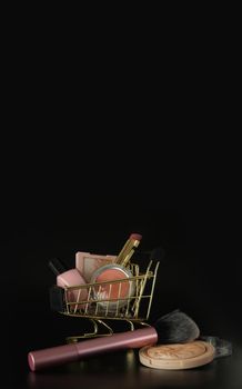 Shopping trolley full of make up and cosmetic goods on black background. Black friday concept. Sale and discount. Goods for women. Closeup of a basket with products for make-up. Beauty background, free space for text, copy space, modern layout, close up.